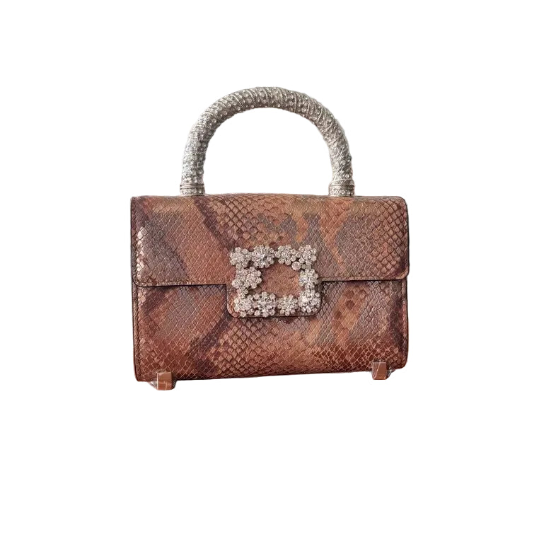 A brown leather handbag with a chain link embellishment on the front, displayed on a wooden table.