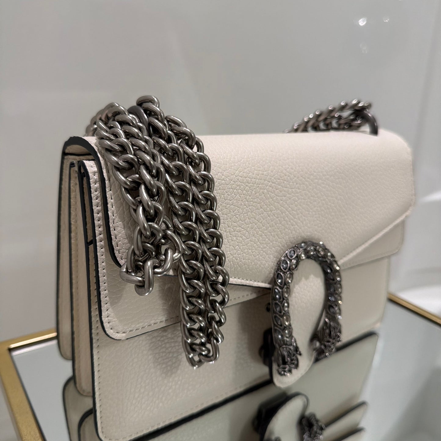 Beige handbag with a chain detail on a white surface