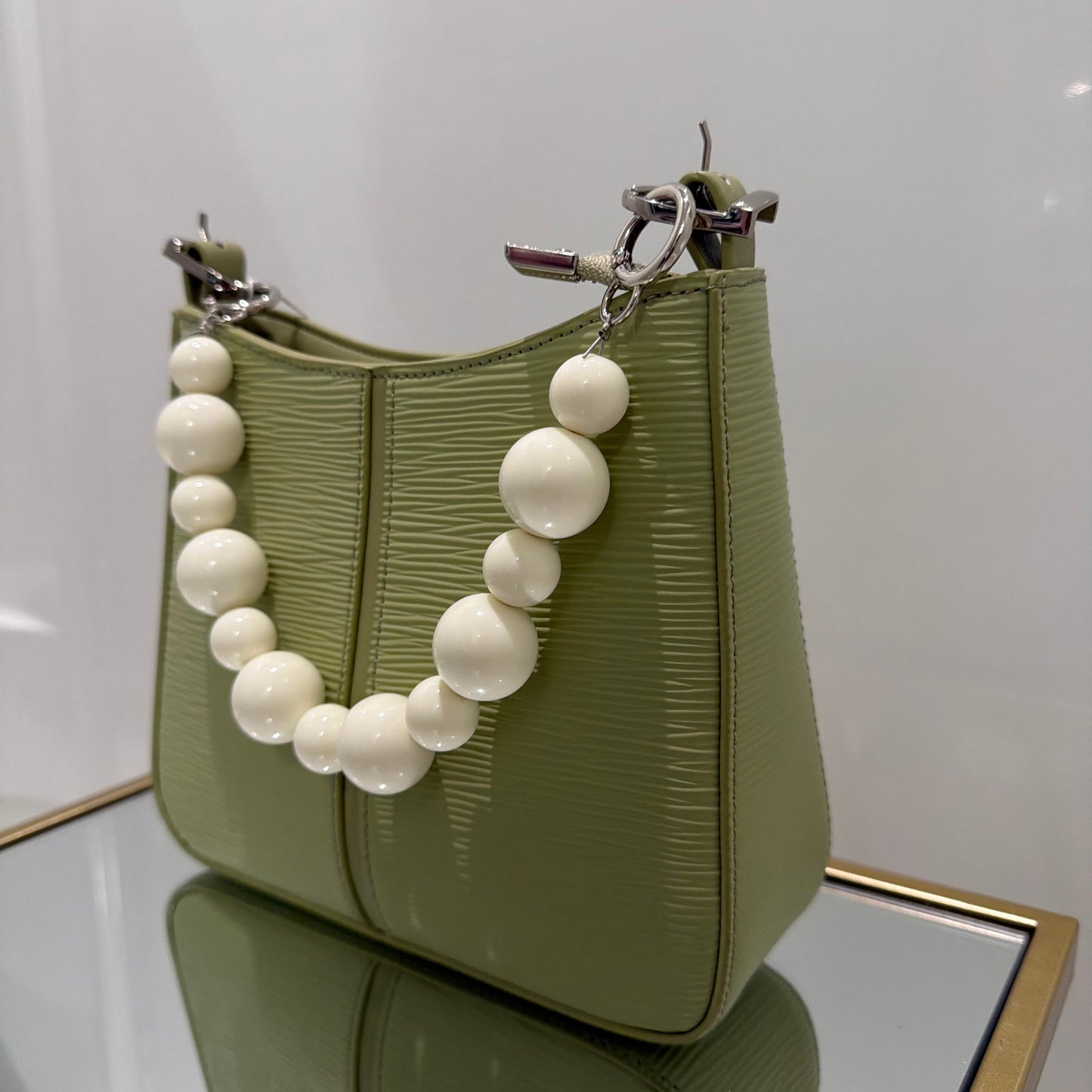 Green handbag with a white beaded strap on a white background
