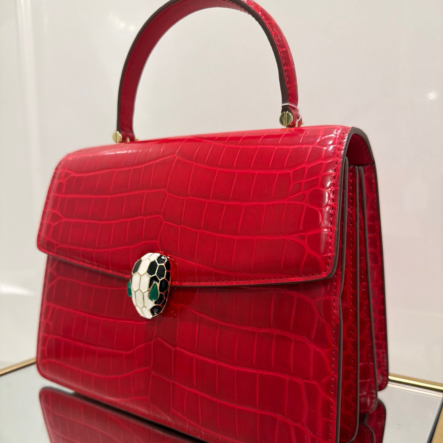 Red crocodile-patterned handbag with a decorative clasp on a white background