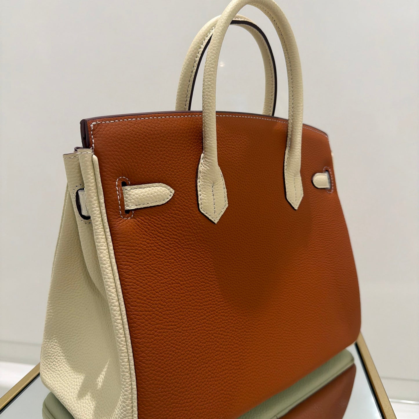 Brown leather handbag with beige handles and trim on a white background