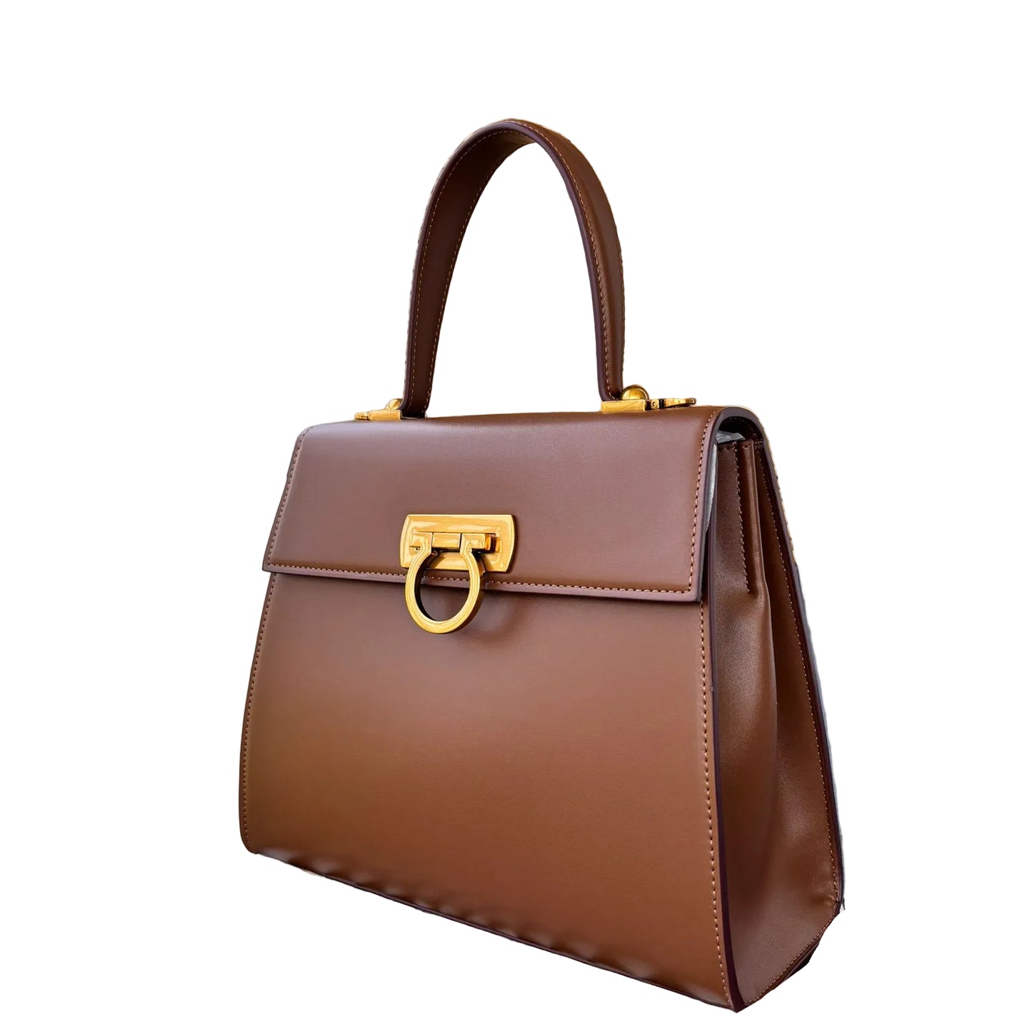 A luxurious brown leather handbag with a structured silhouette, featuring a gold-toned hardware clasp and a sturdy top handle, displayed on a table with a woven wall decor in the background.