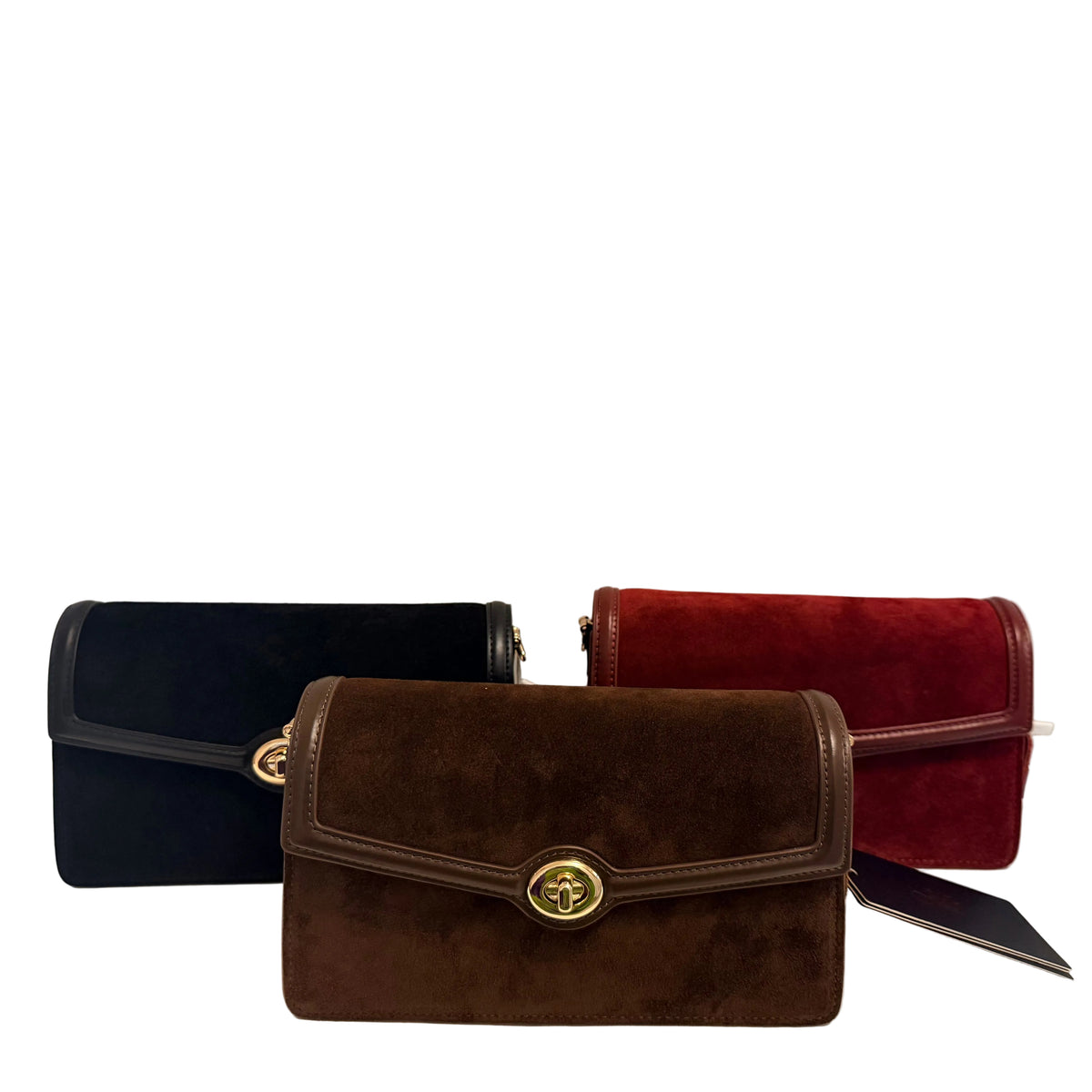 Three suede flap shoulder bags in black, brown, and red, arranged side-by-side on a white surface against a plain light gray wall. The center brown bag is in sharp focus in the foreground, while the other two are slightly blurred in the background.