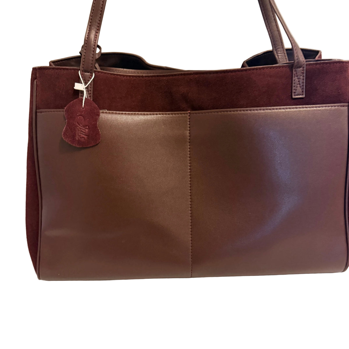 A brown leather and suede tote bag with dual shoulder straps, a hanging leather tag, and a front panel divided by a vertical seam, photographed against a plain light background.