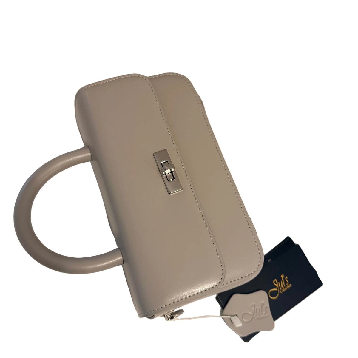 A light gray structured handbag with a top handle, silver clasp, and a dark blue dust bag with gold lettering, placed on a white surface.