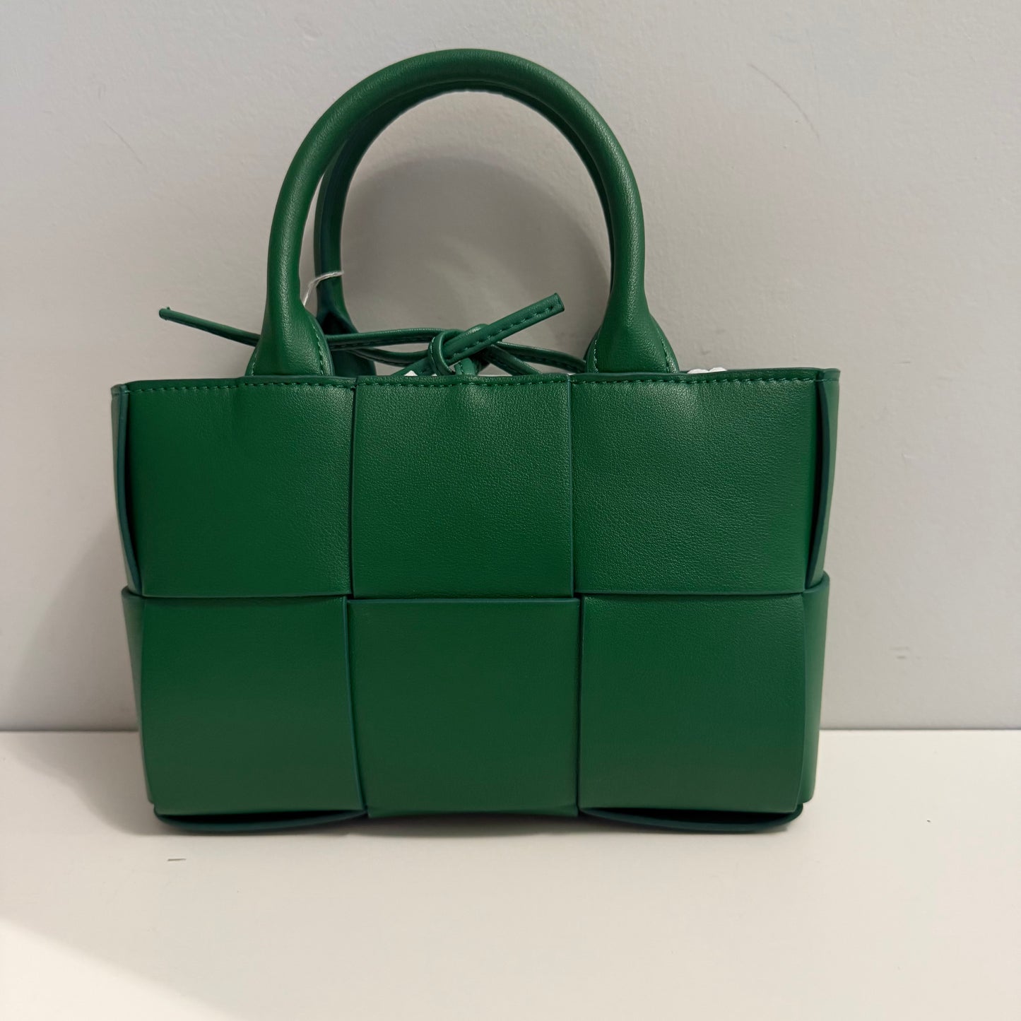 Green woven handbag on a white surface with a light gray background