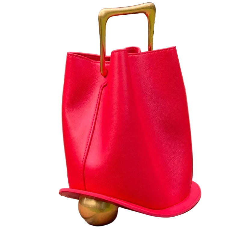 Red handbag with gold handle and base on a brick ledge in an outdoor setting