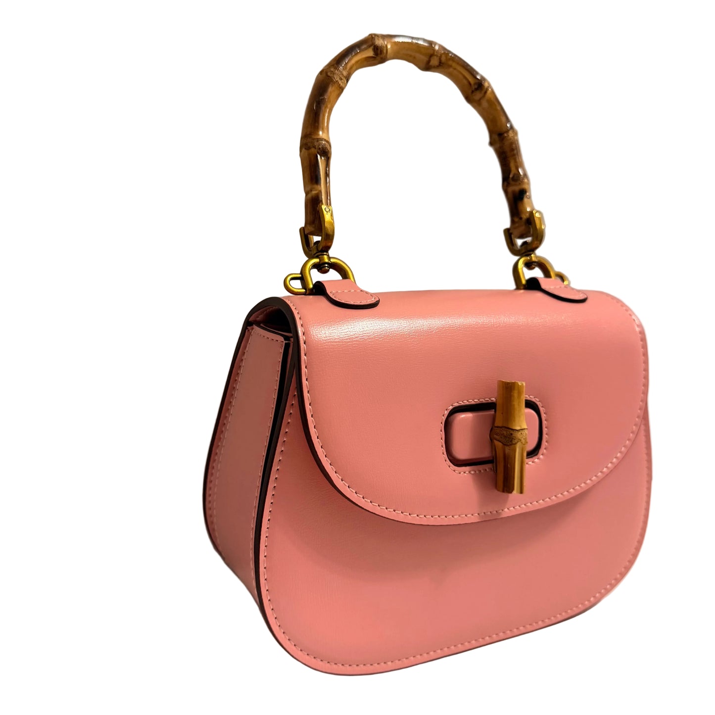Pink handbag with gold bamboo handle and hardware on a neutral background
