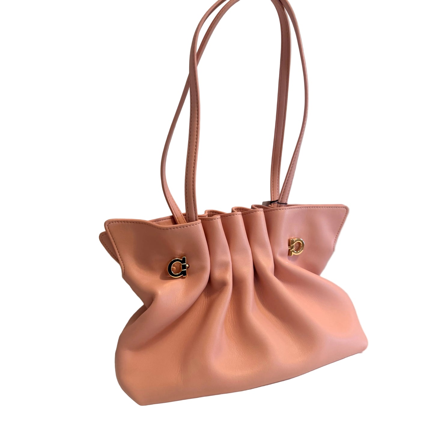 A blush pink leather handbag with gathered draping details, dual shoulder straps, and gold-tone hardware, resting on a white surface against a light gray wall.