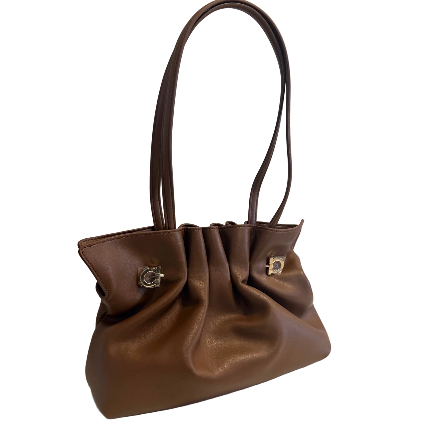A brown leather shoulder bag with a gathered, slouchy silhouette, dual top handles, and silver-tone hardware, resting on a white surface against a light gray wall.
