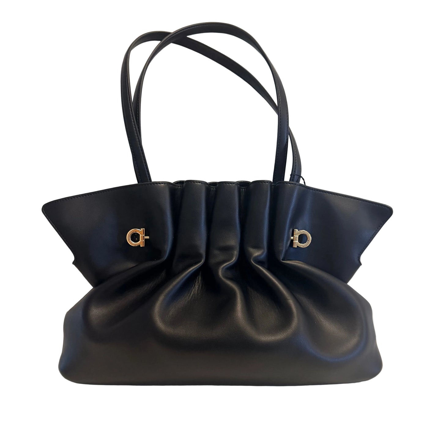 A black leather handbag with gathered pleats and two gold-tone Gancini logo hardware accents, displayed on a white surface against a white wall.