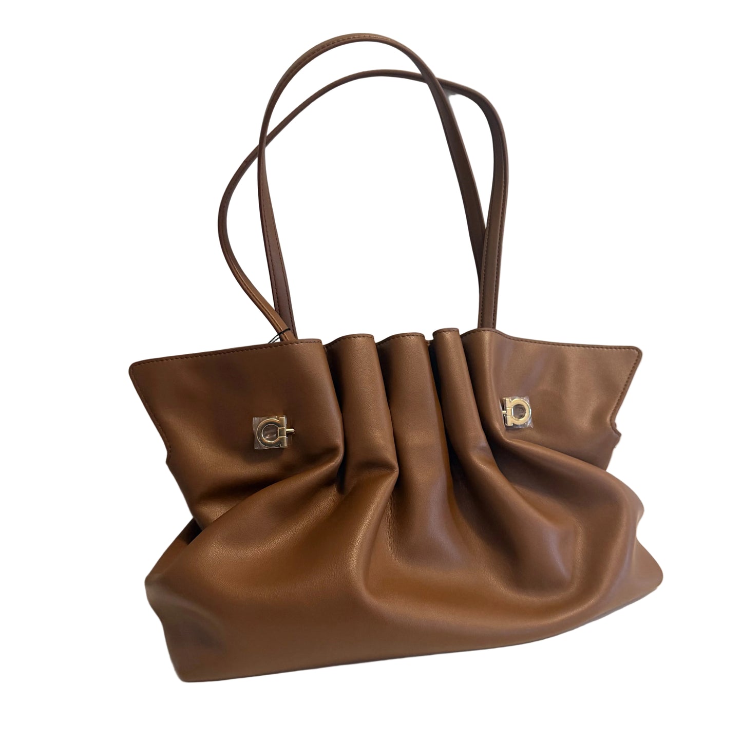 A brown leather slouchy handbag with dual shoulder straps and silver-tone hardware, resting on a white surface against a light gray wall.