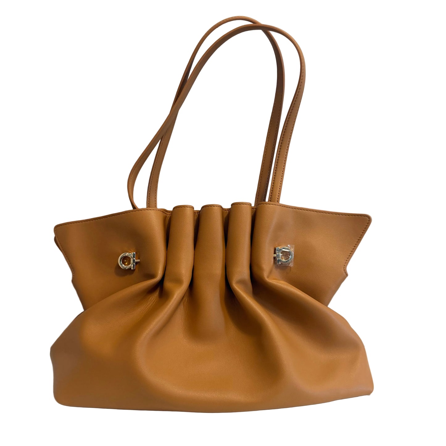 A tan leather handbag with gathered pleats at the top and two silver-tone hardware accents, displayed on a white surface against a light gray wall.