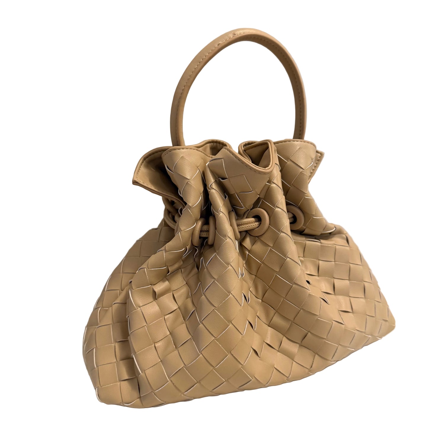 A beige woven leather handbag with a single top handle, photographed on a white surface against a plain light gray wall.