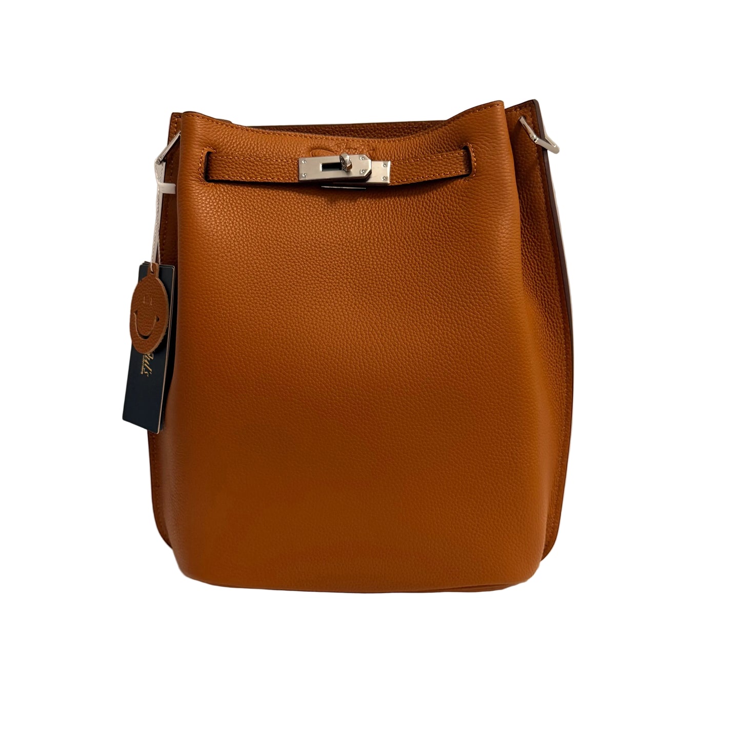 A tan pebbled leather bucket bag with silver-tone hardware, shown standing upright on a white surface against a light gray background. A blue hangtag is attached on the left side.