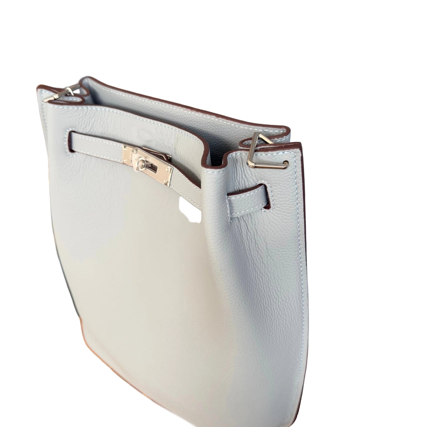 A light gray pebbled leather handbag with silver-tone hardware, resting on a wooden surface against a gray paneled background.
