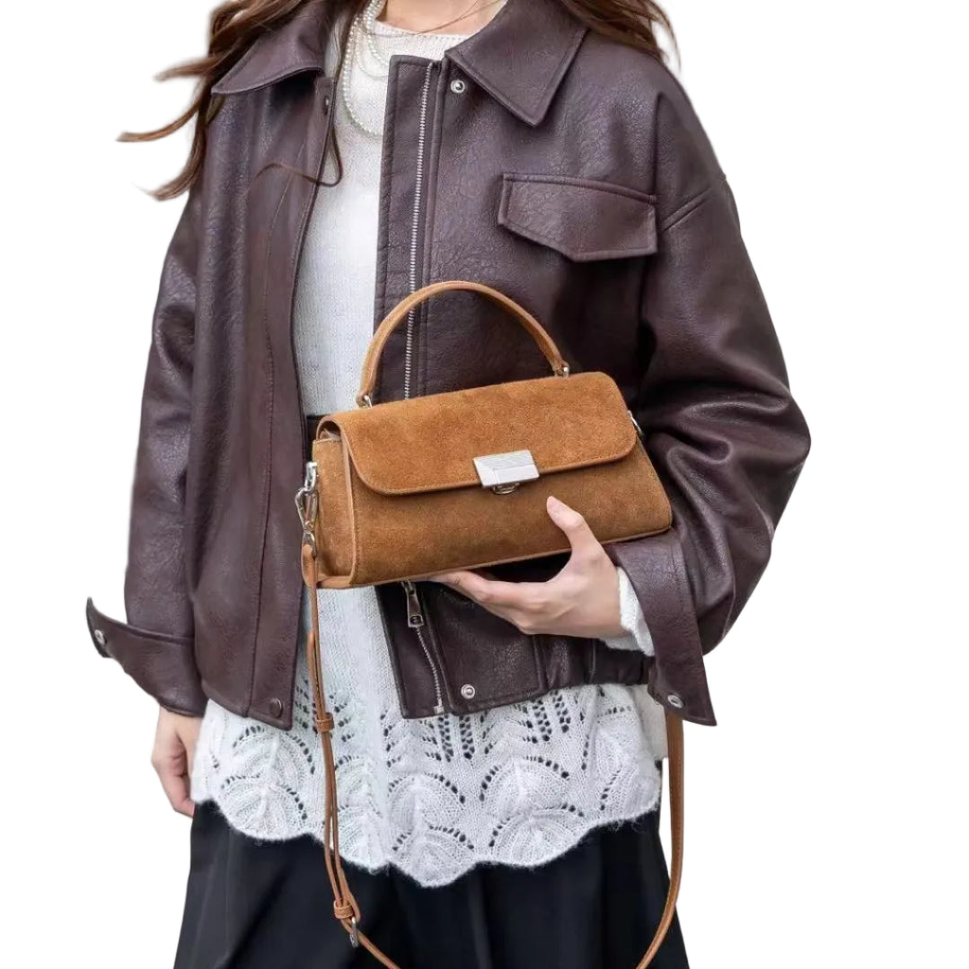 A person wearing a dark brown faux-leather jacket, a white lace-trimmed top, black wide-leg pants, and holding a brown suede top-handle handbag with a tan shoulder strap.