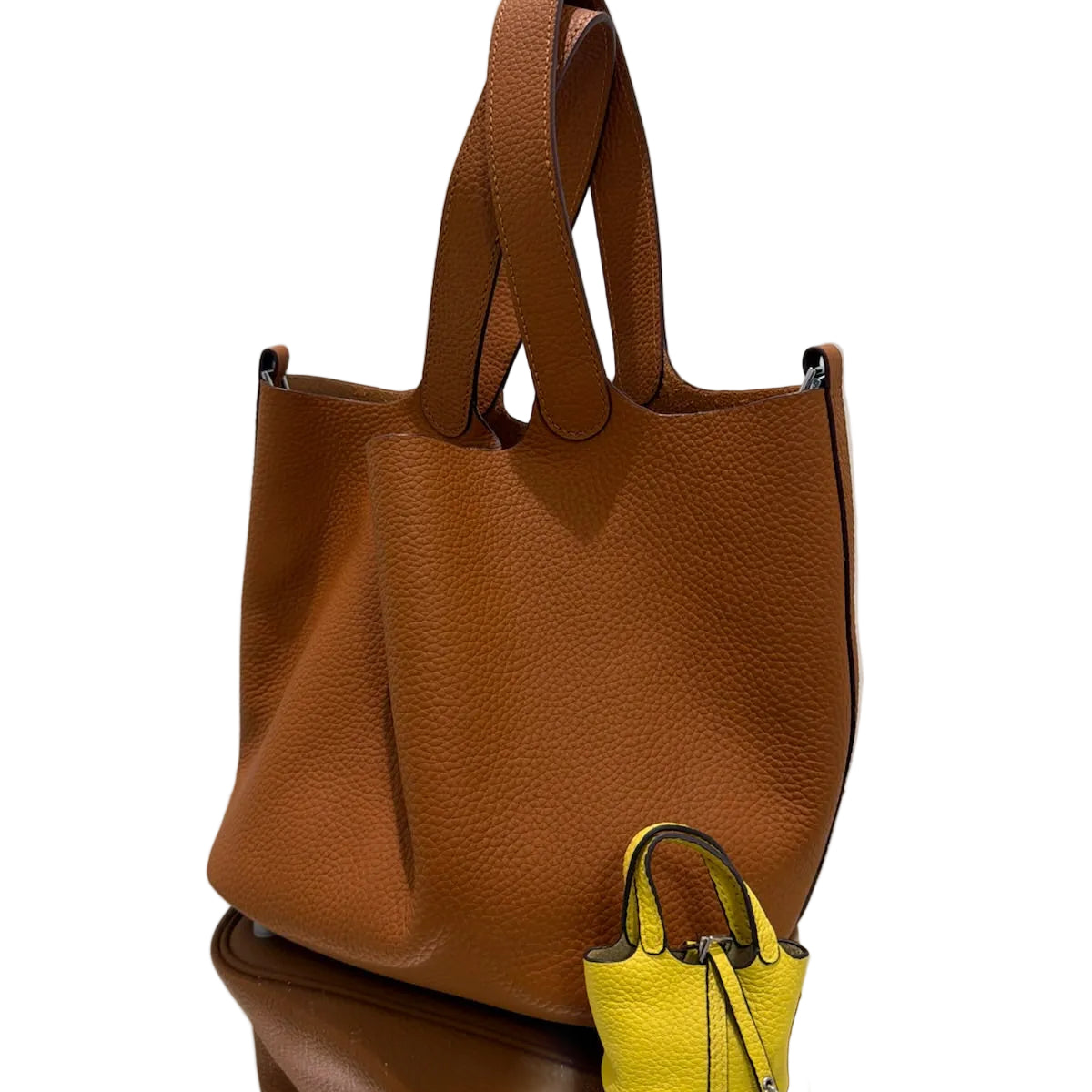 Brown leather tote bag on a reflective surface with a white background