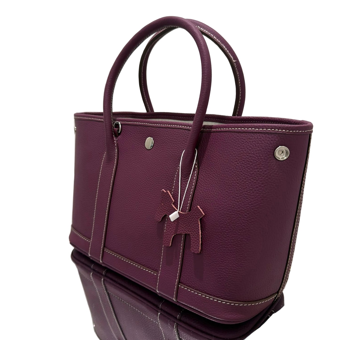 Purple leather handbag on a reflective surface with a white background