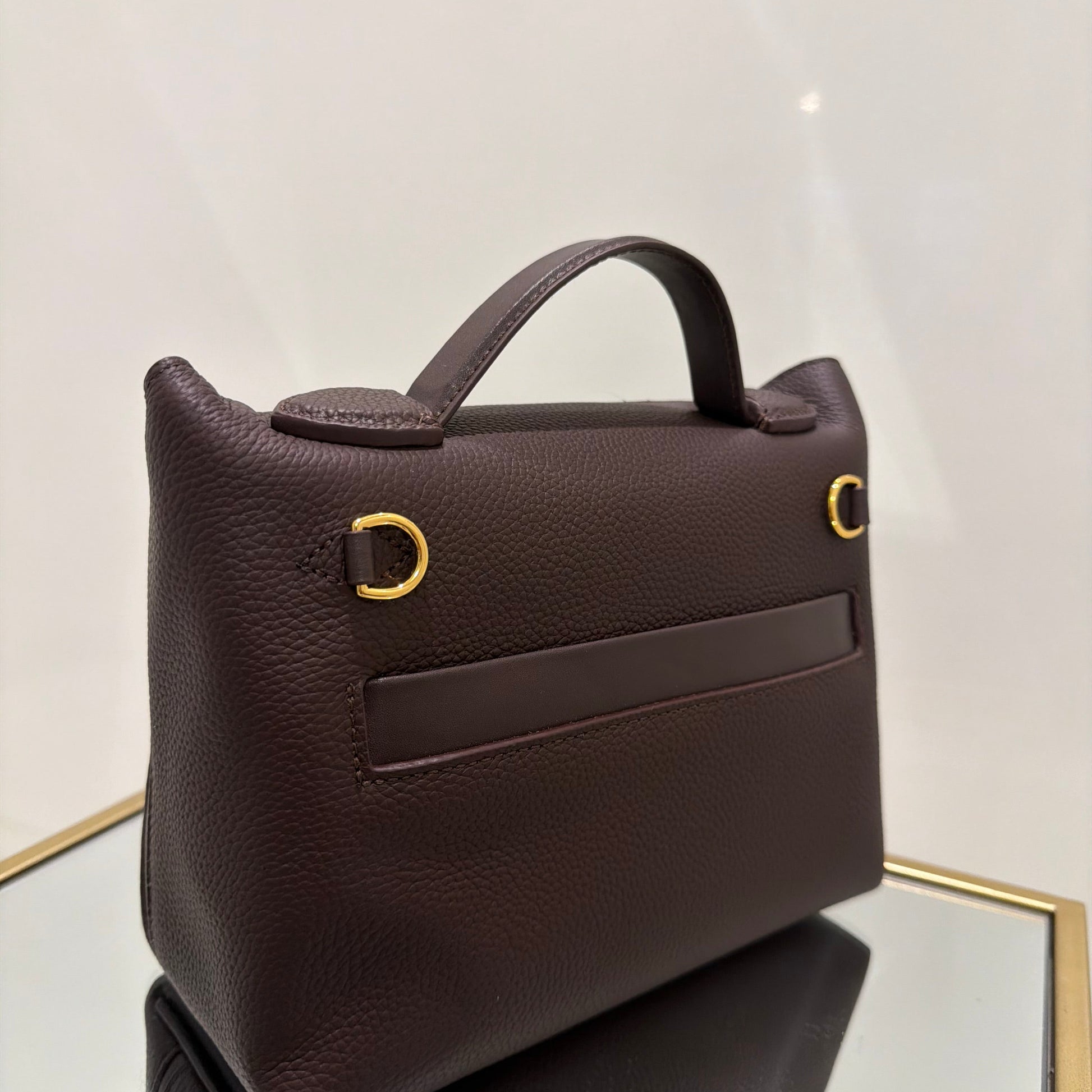 Brown leather handbag with gold accents on a light gray background