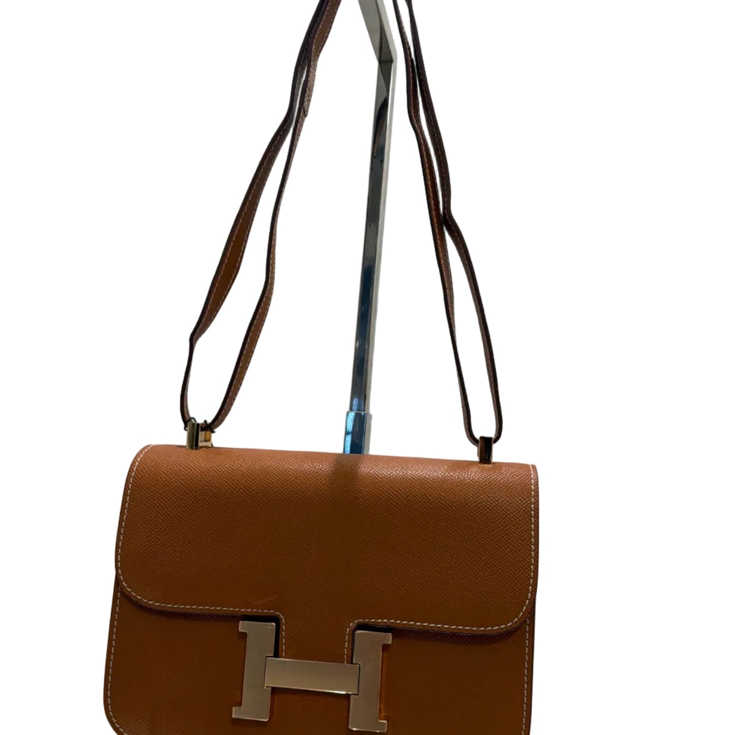 Brown leather handbag with gold 'H' logo on a reflective surface