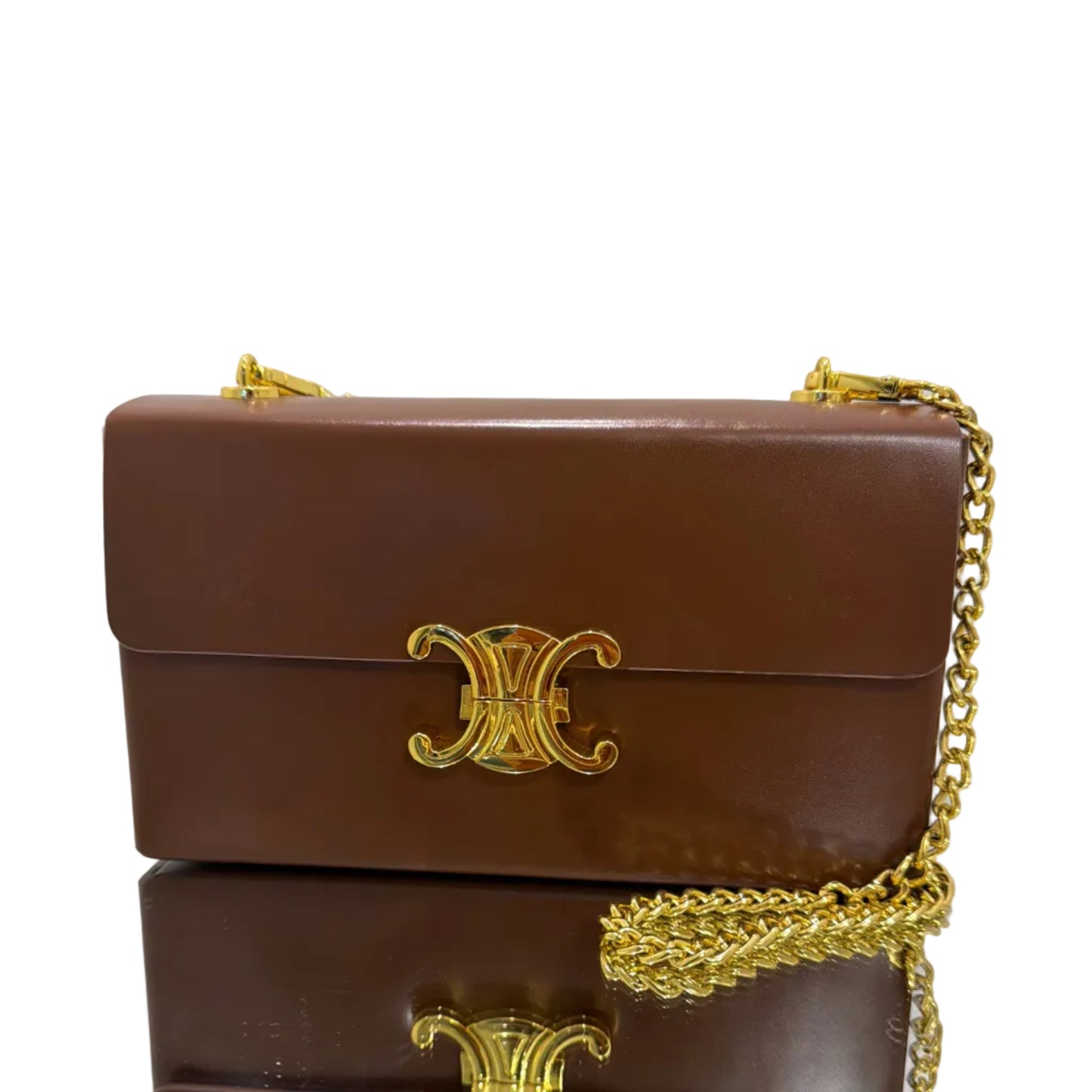 Brown leather handbag with gold chain and decorative clasp on a light gray background