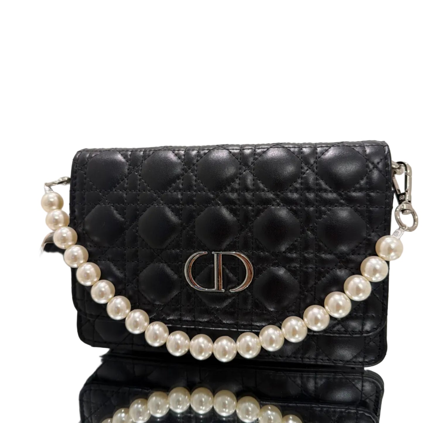 Black quilted handbag with a pearl strap on a reflective surface