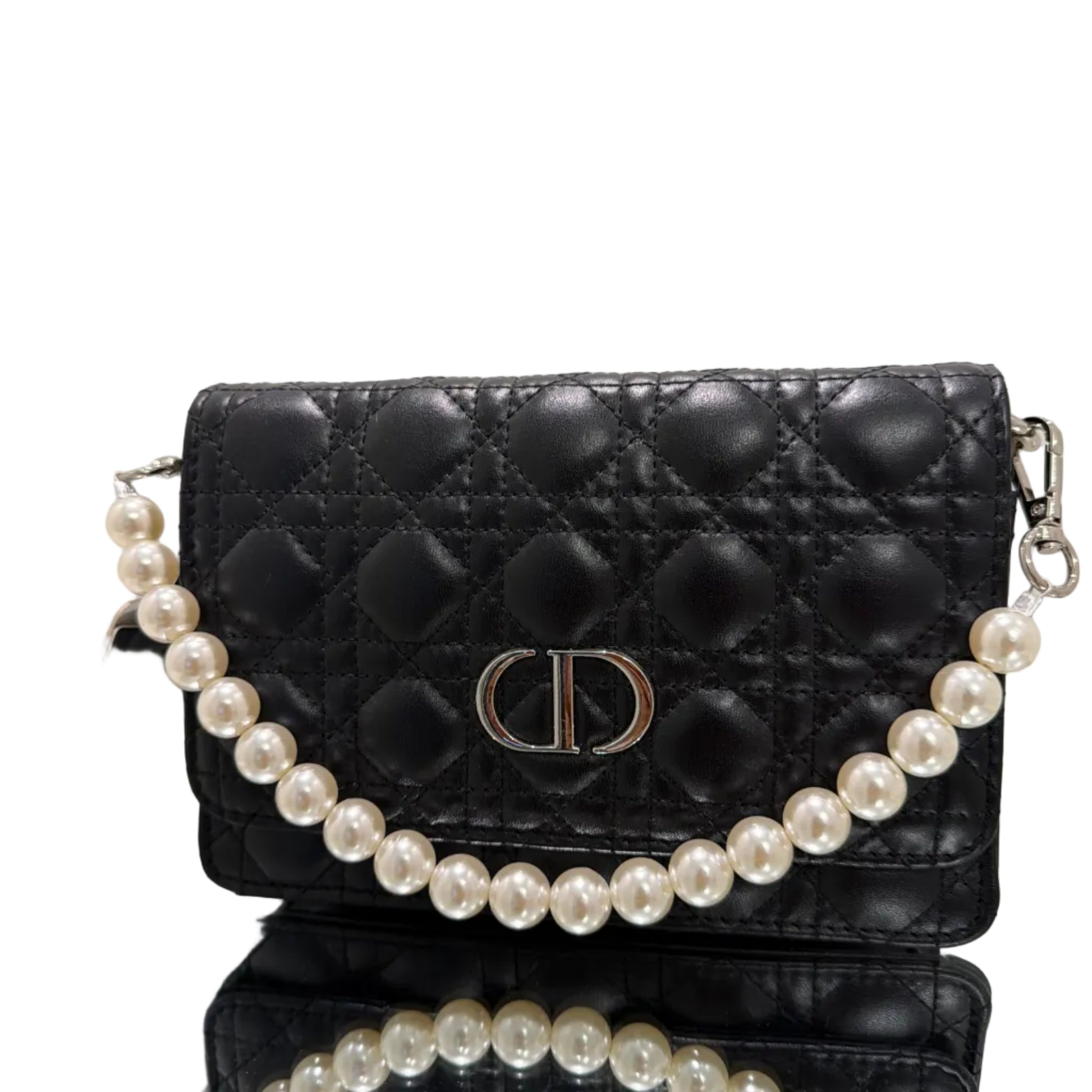 Black quilted handbag with a pearl strap on a reflective surface