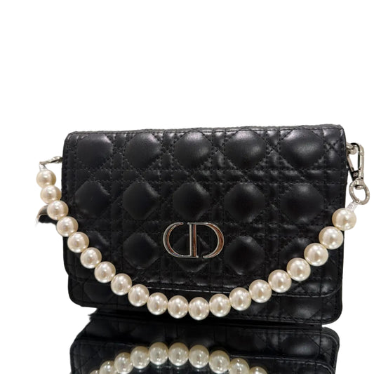 Black quilted handbag with a pearl strap on a reflective surface