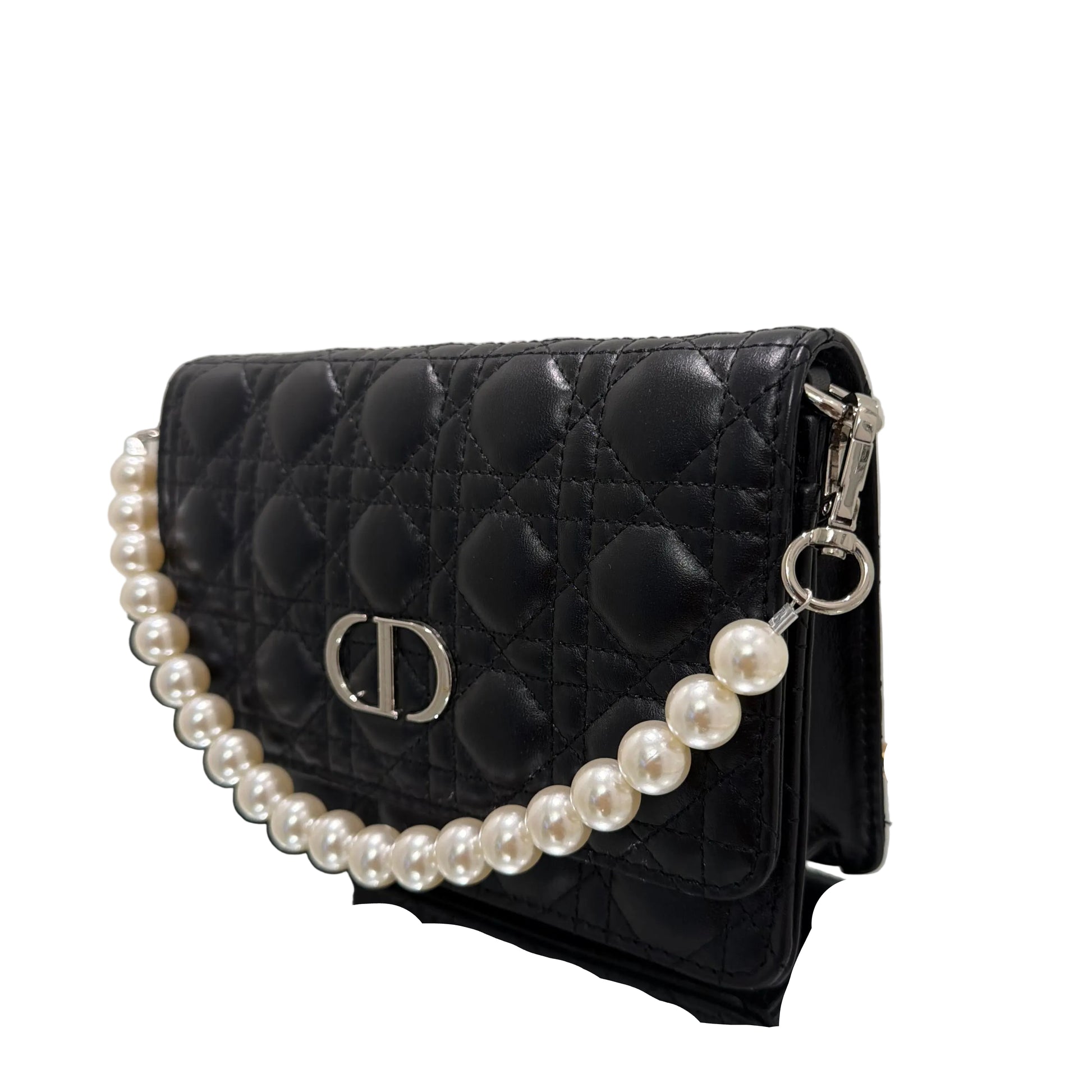 Black quilted handbag with a pearl necklace draped over it on a white background