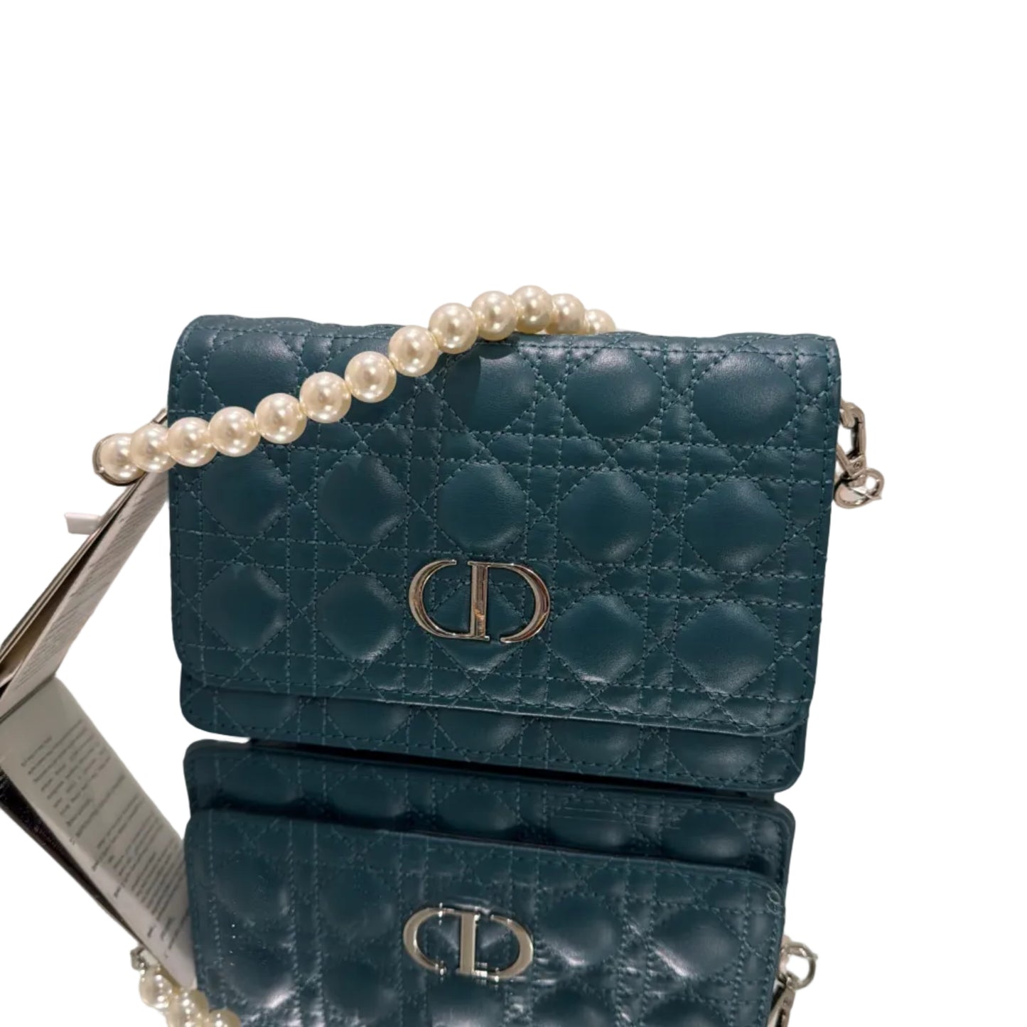 Blue quilted handbag with a pearl strand on a stand against a neutral background