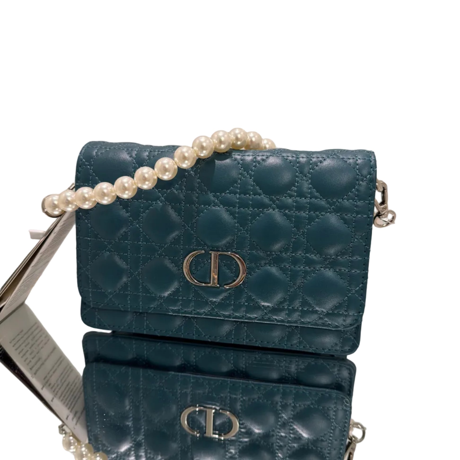 Blue quilted handbag with a pearl strand on a stand against a neutral background