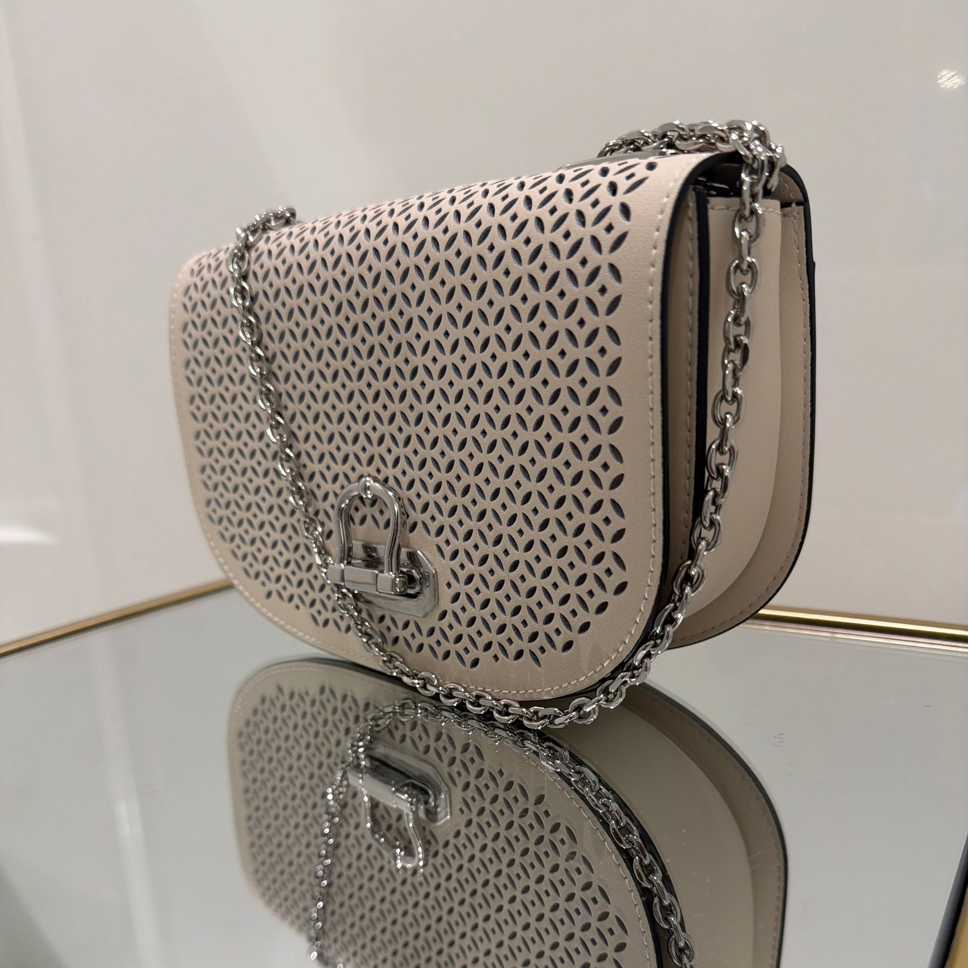 Two beige handbags with intricate patterns and chains on a white surface.