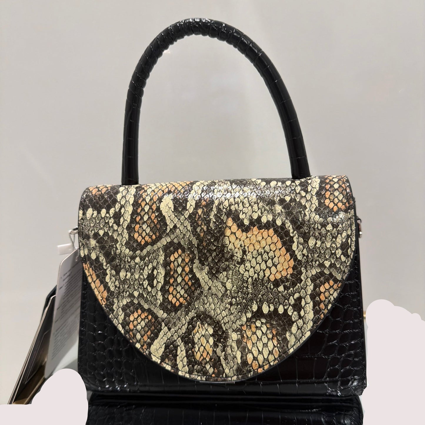 Black handbag with snake skin pattern on a light gray background