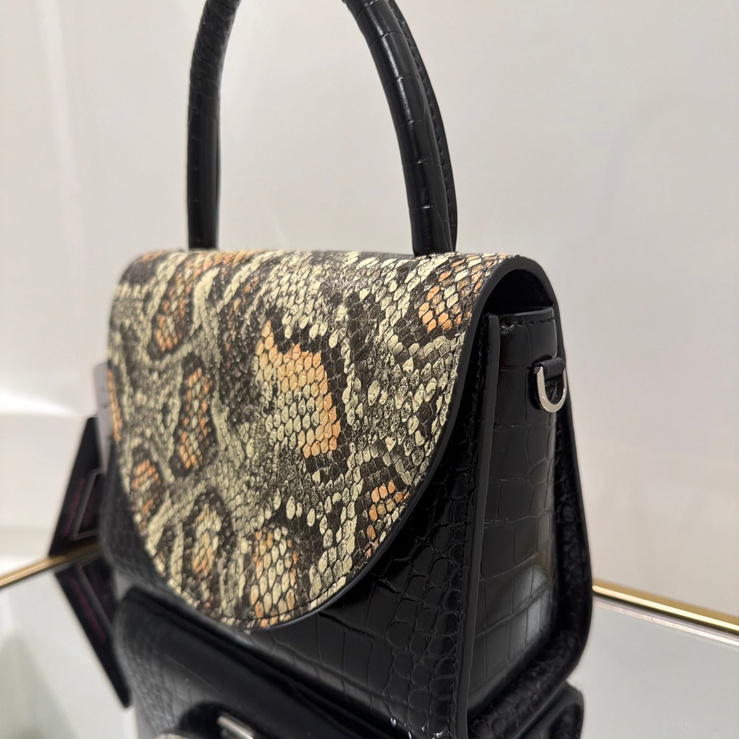 Black handbag with snake print handle on a white background