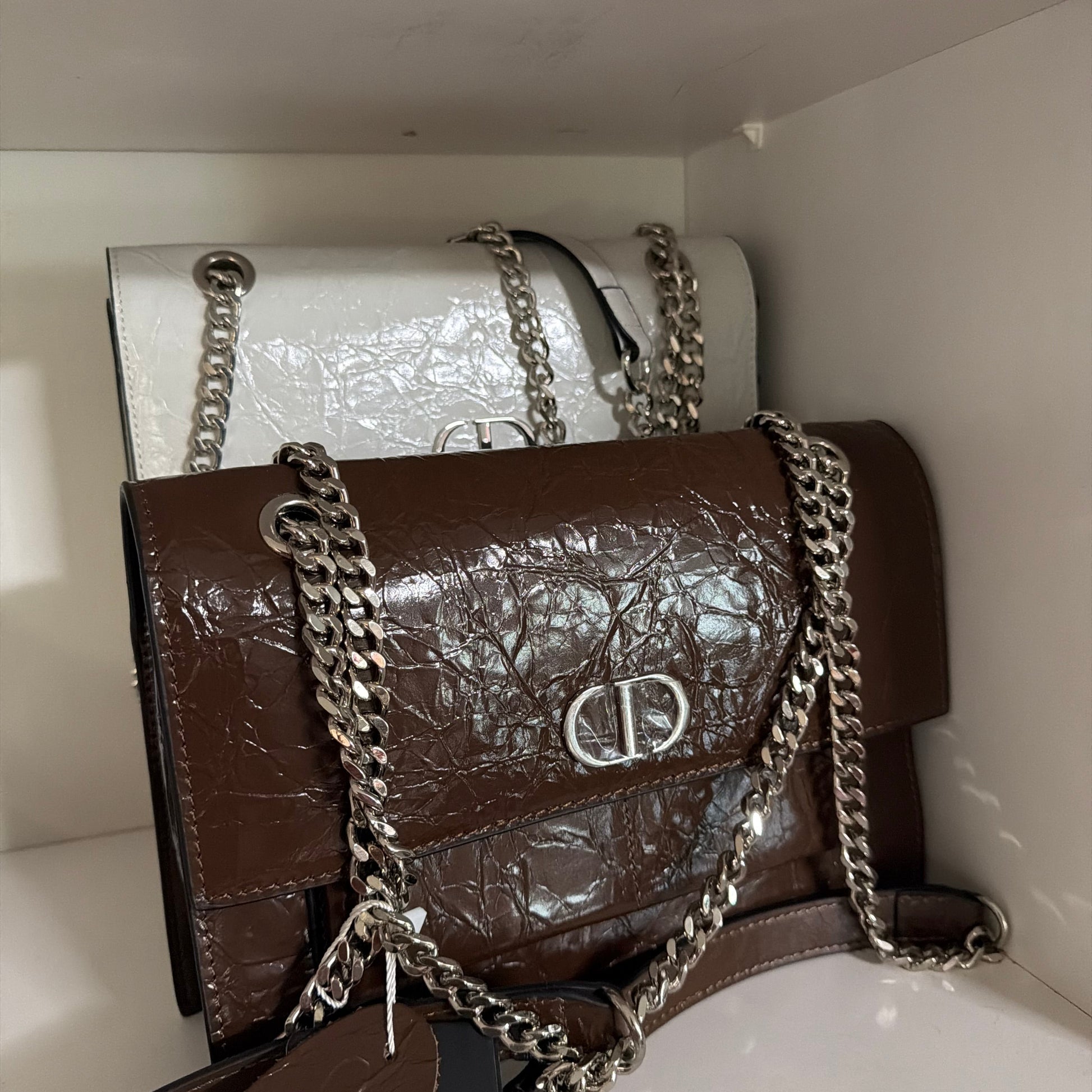 Two handbags, one brown and one white, with chains on a white background.