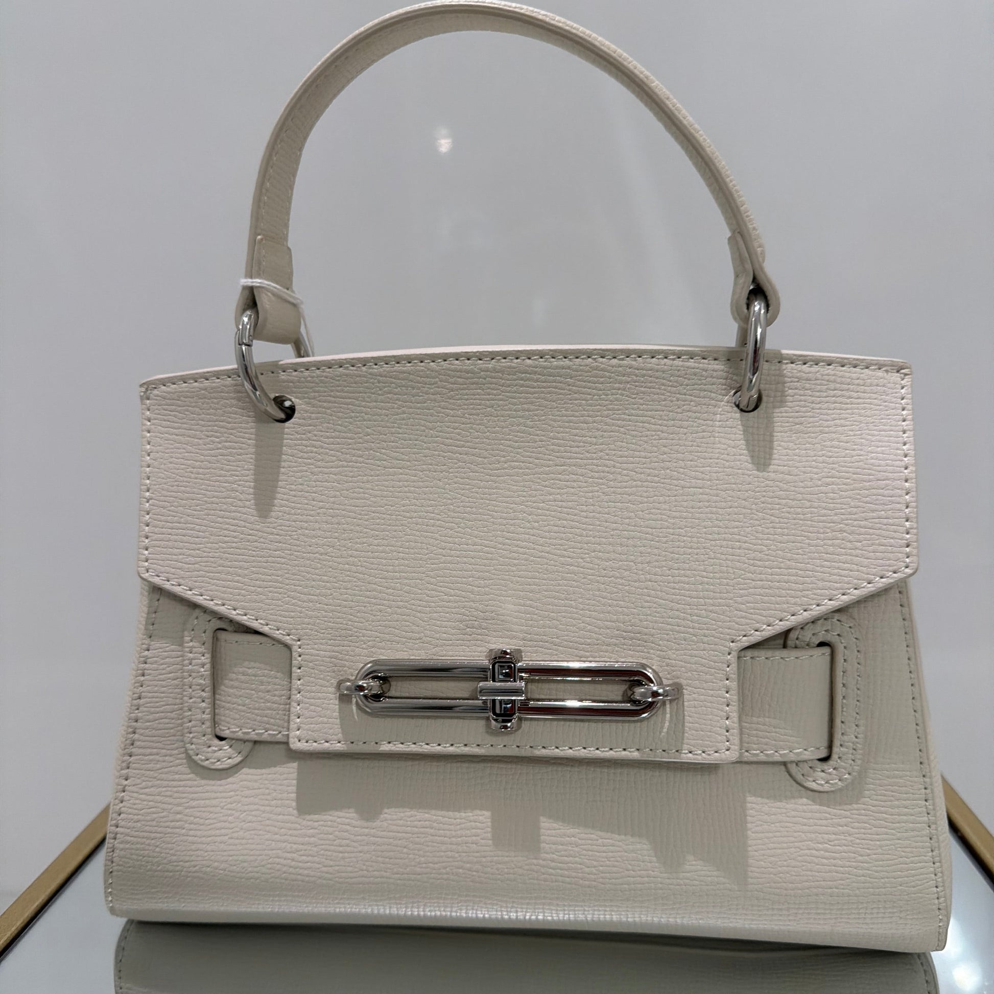 Light gray handbag with a metal clasp on a light gray background