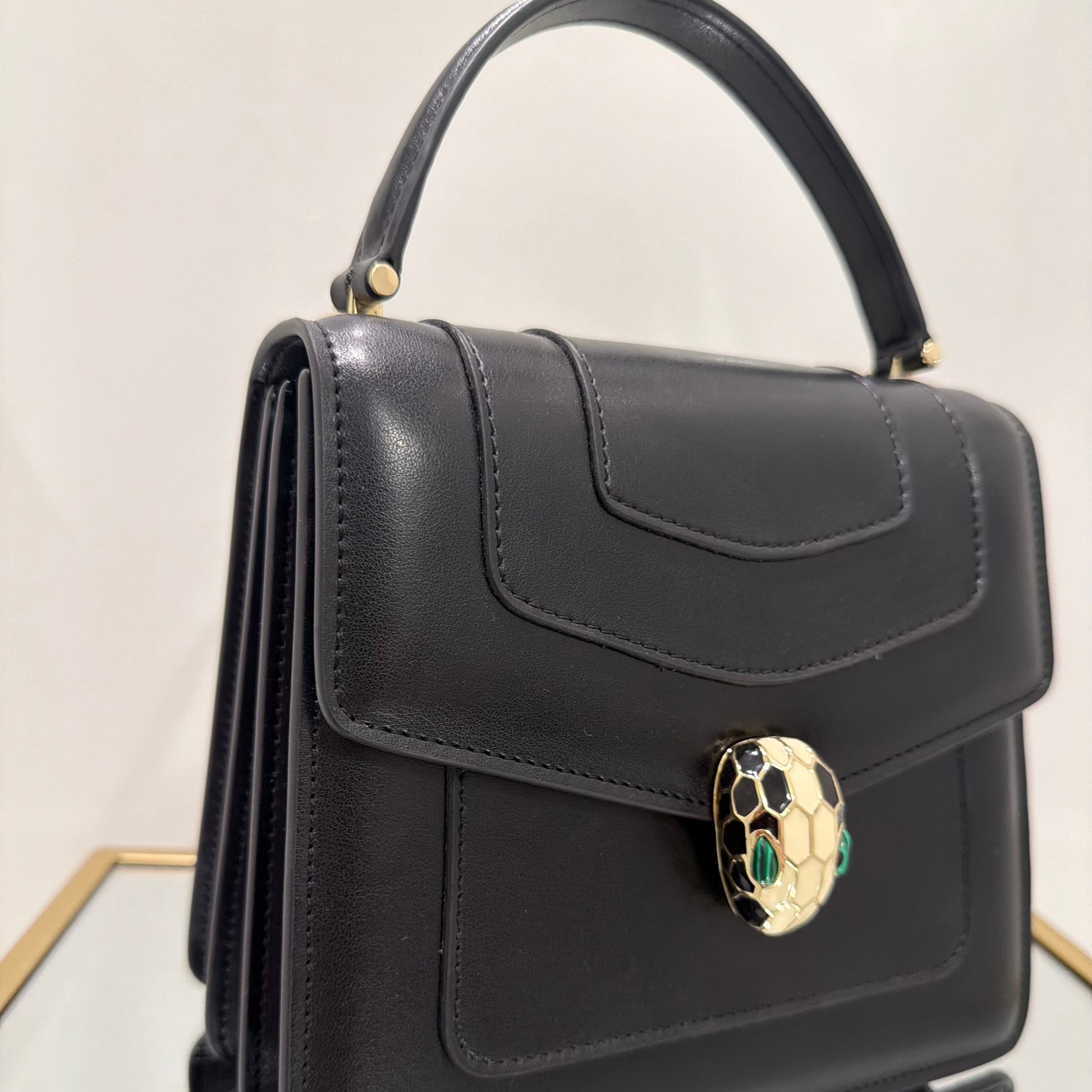Black handbag with a decorative clasp on a light background