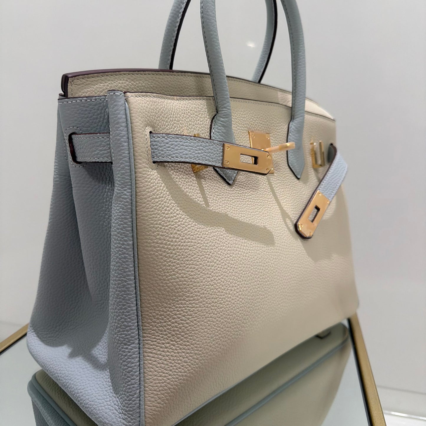 Two-tone handbag with gold hardware on a reflective surface