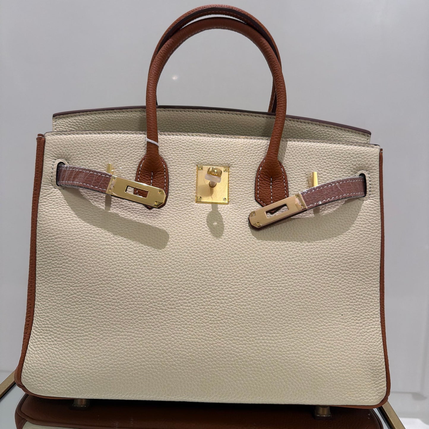 Beige handbag with brown handles and trim on a white background