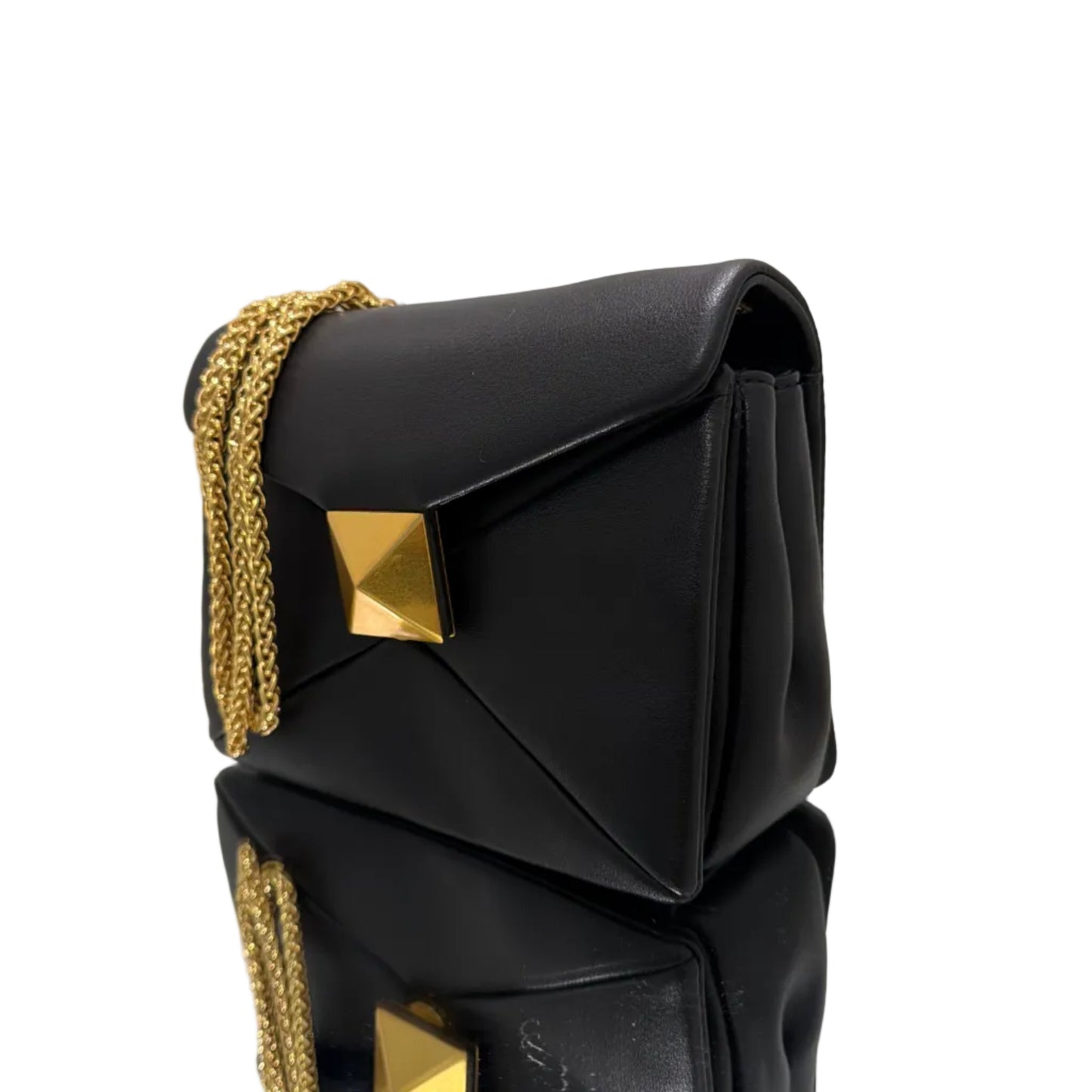 Black clutch bag with gold chain and studs on a white surface