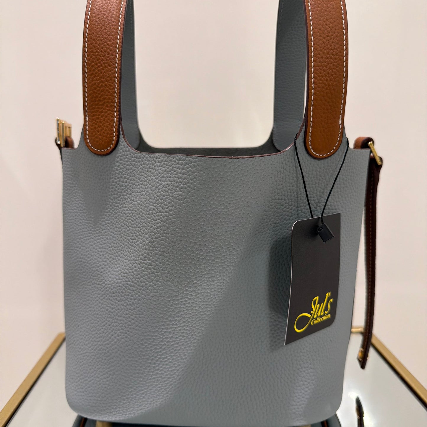 Gray handbag with brown handles and a visible brand tag on a light background