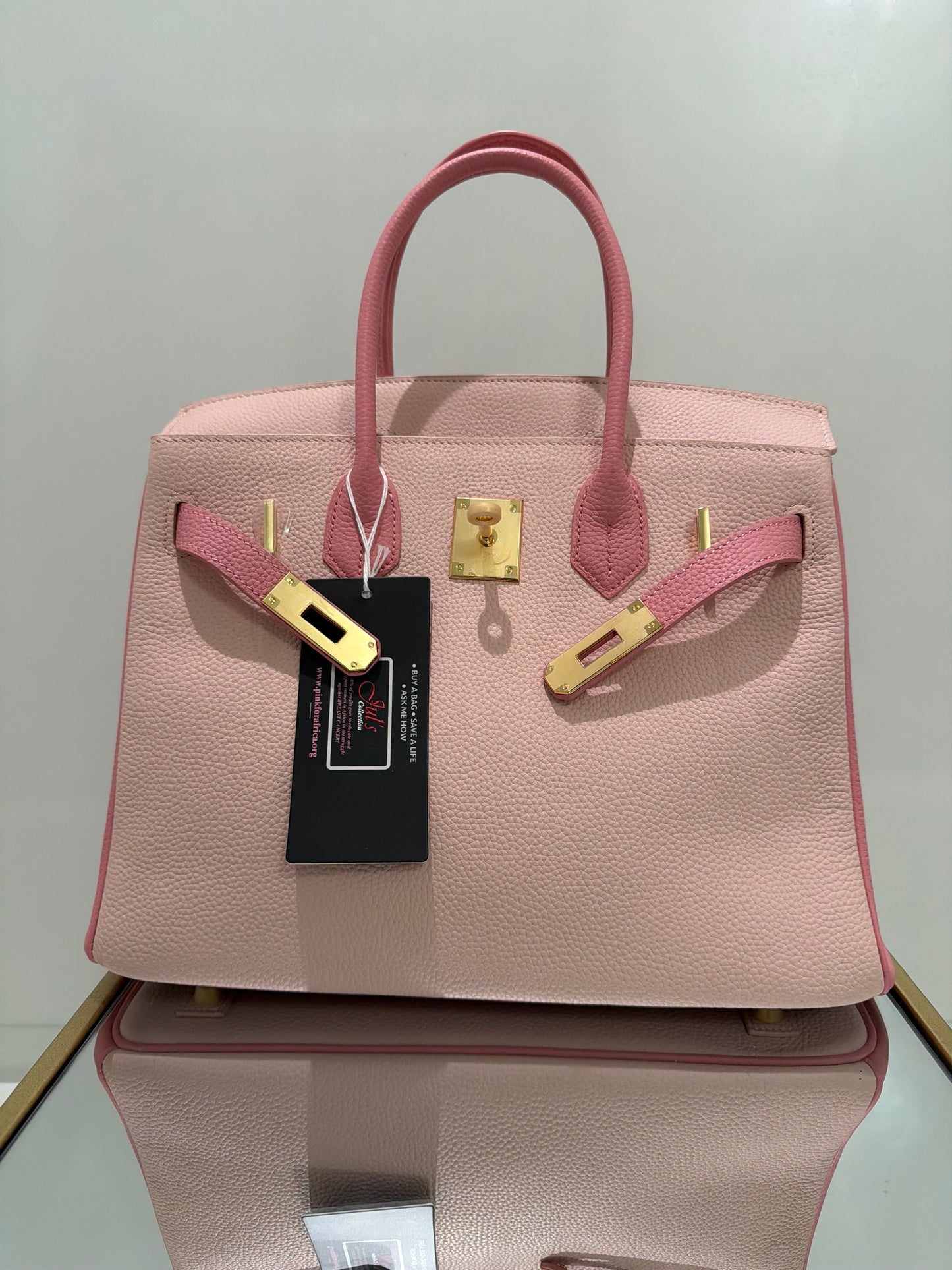 Pink handbag with gold accents and a visible brand tag on a light gray background