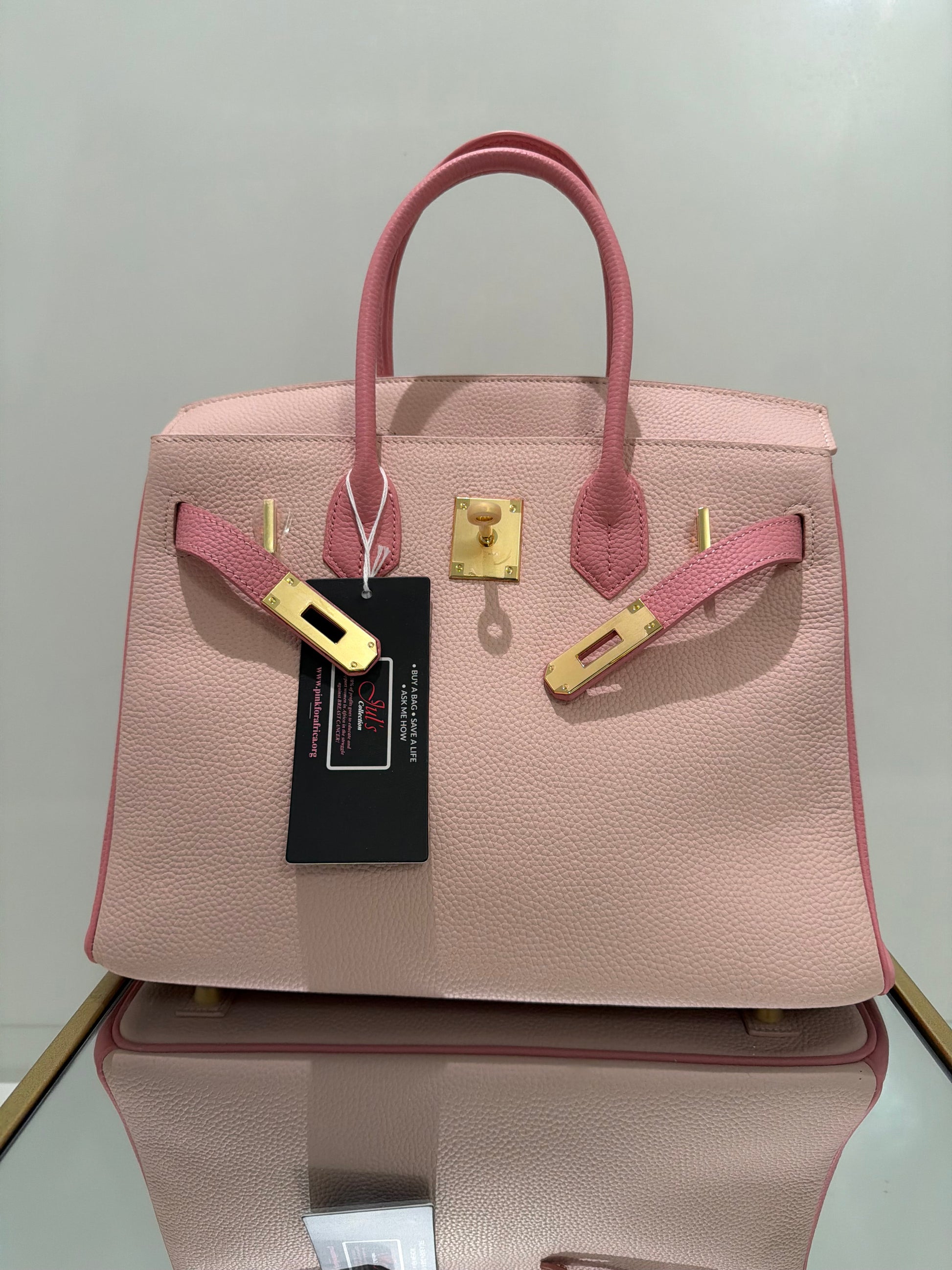 Pink handbag with gold accents and a visible brand tag on a light gray background