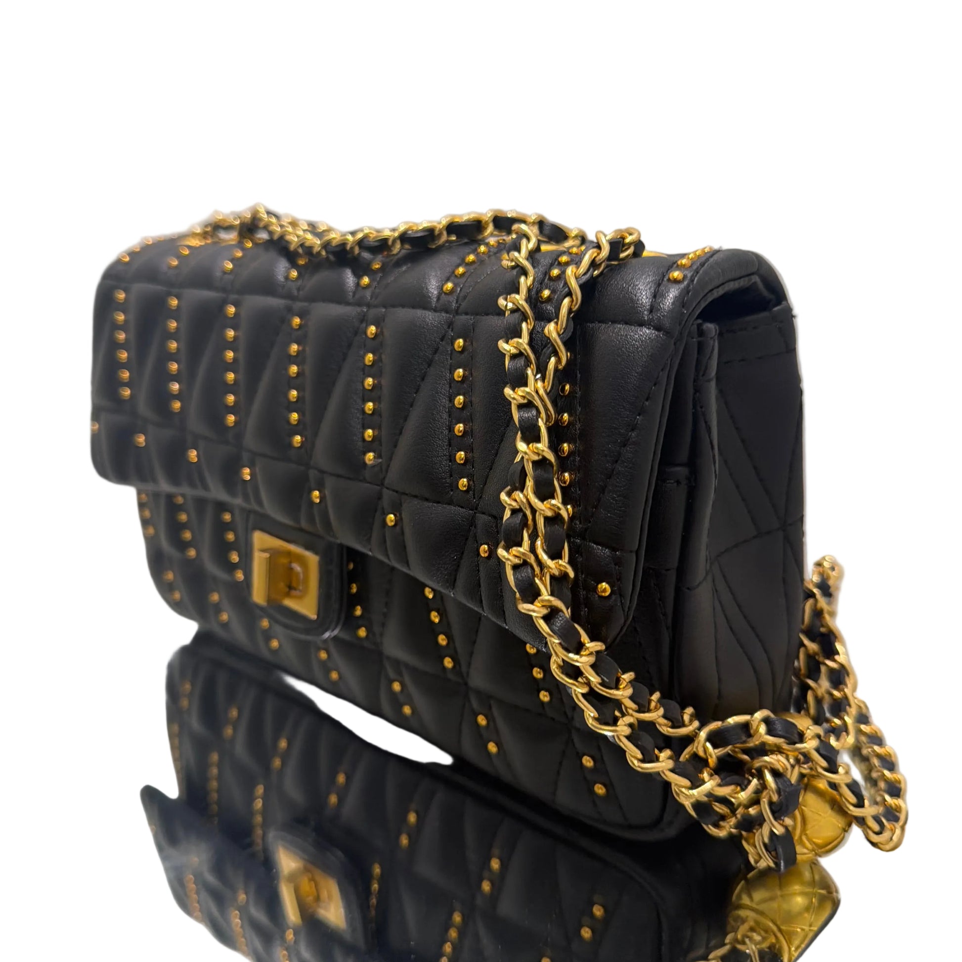 Black quilted handbag with gold chain and studs on a white surface