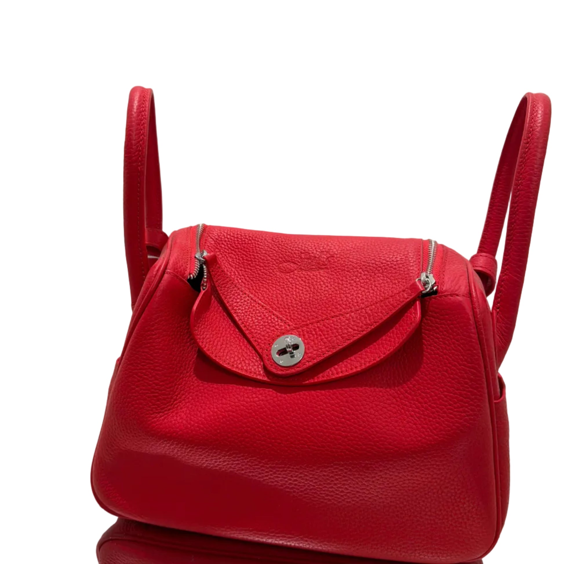 Red leather handbag on a white surface with a gold frame in the background