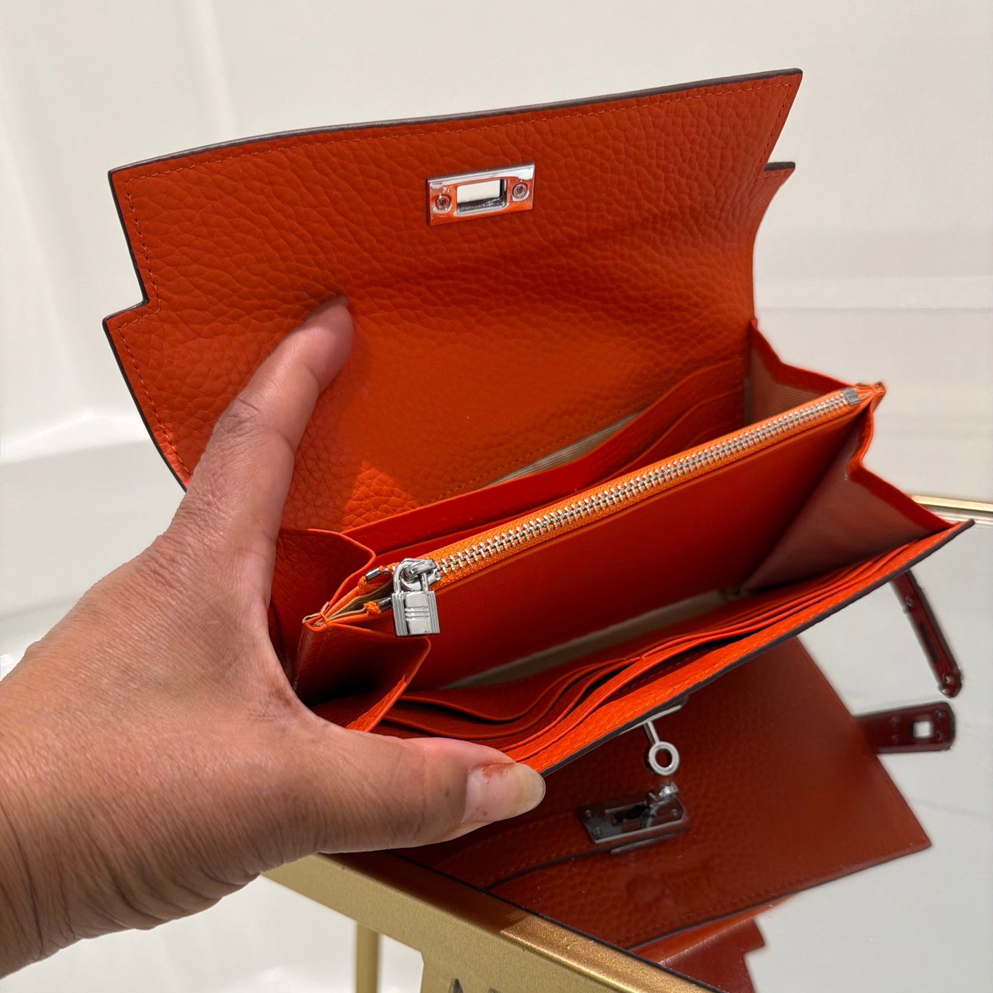 Hand holding an open brown leather clutch with a key inside, on a light background.