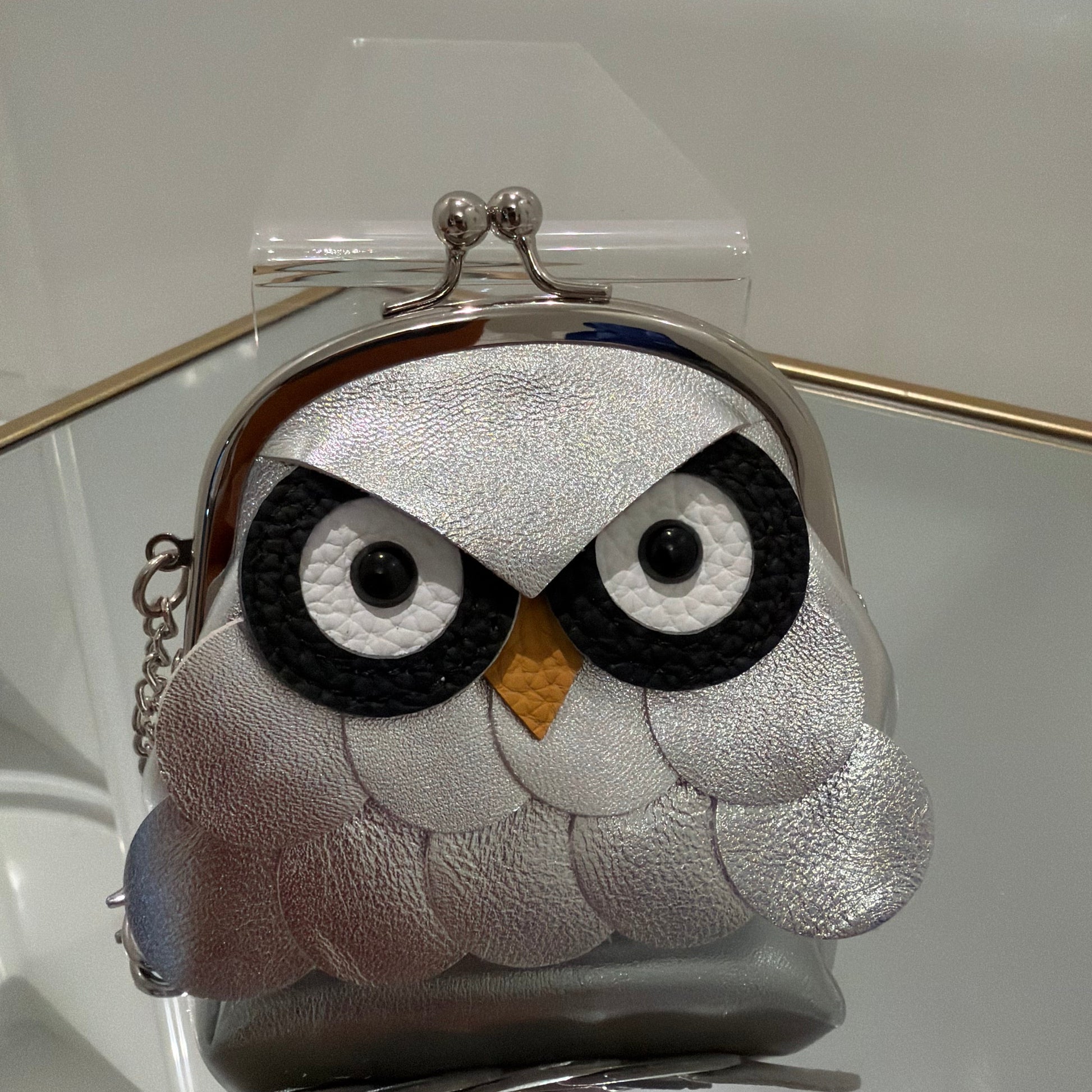 Purse designed like a penguin with silver, black, and white colors on a clear stand.