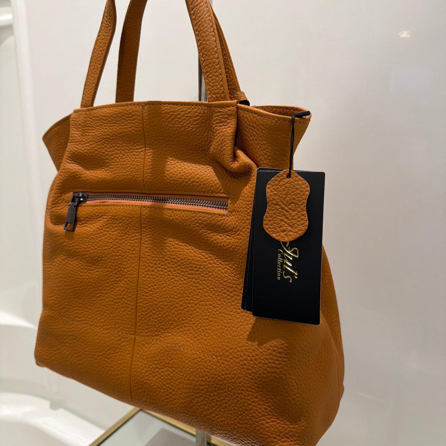 Brown leather handbag with a visible brand tag on a reflective surface.