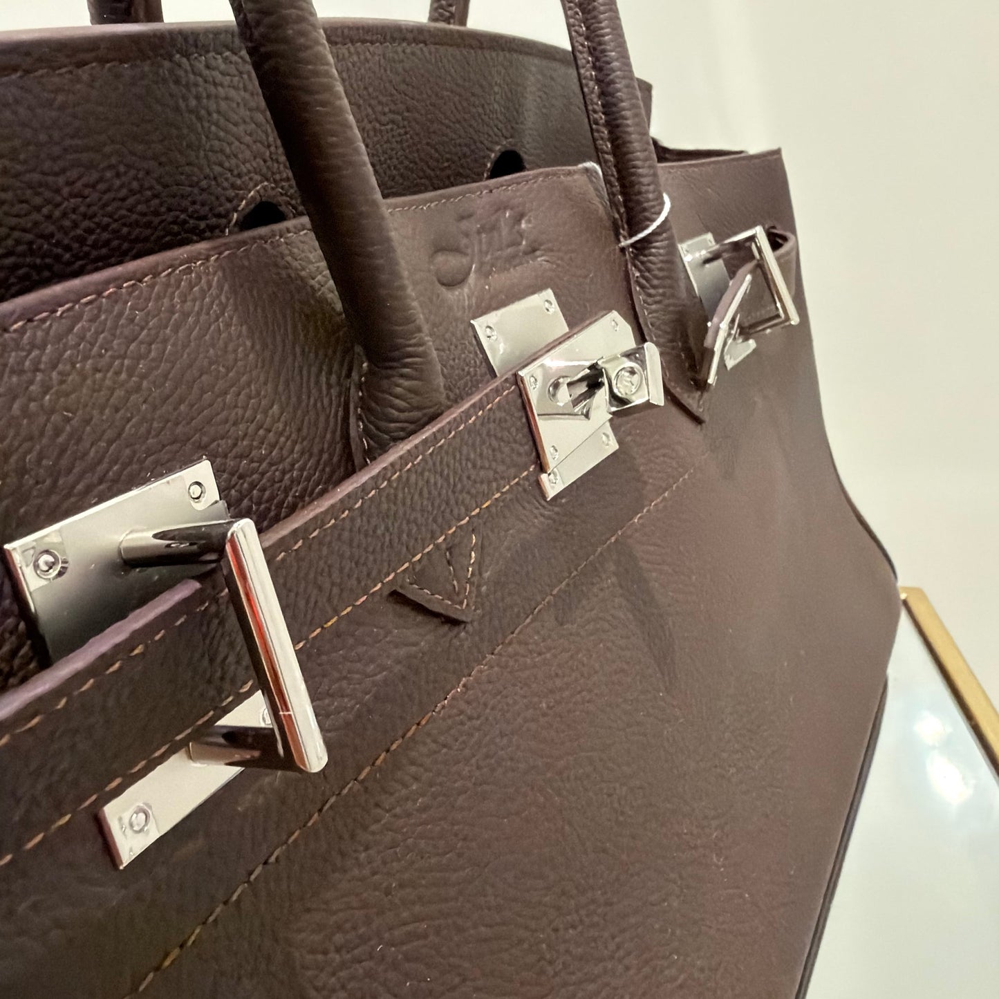 Close-up of a brown leather handbag with silver hardware on a light gray background